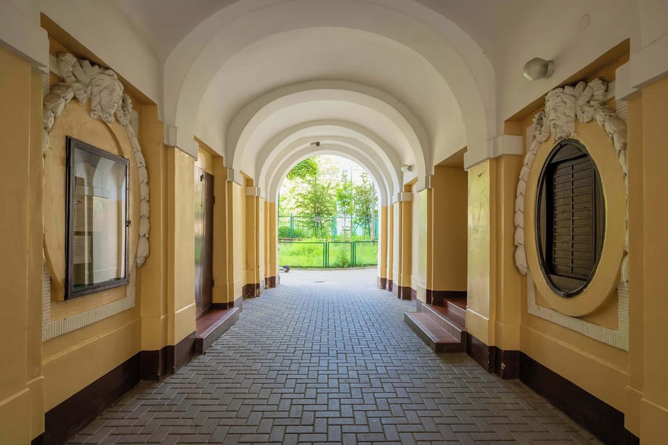 Stylish passageway with arched ceiling, cobblestone floor, and decorative details leads to a green courtyard, creating an elegant entrance to the building.