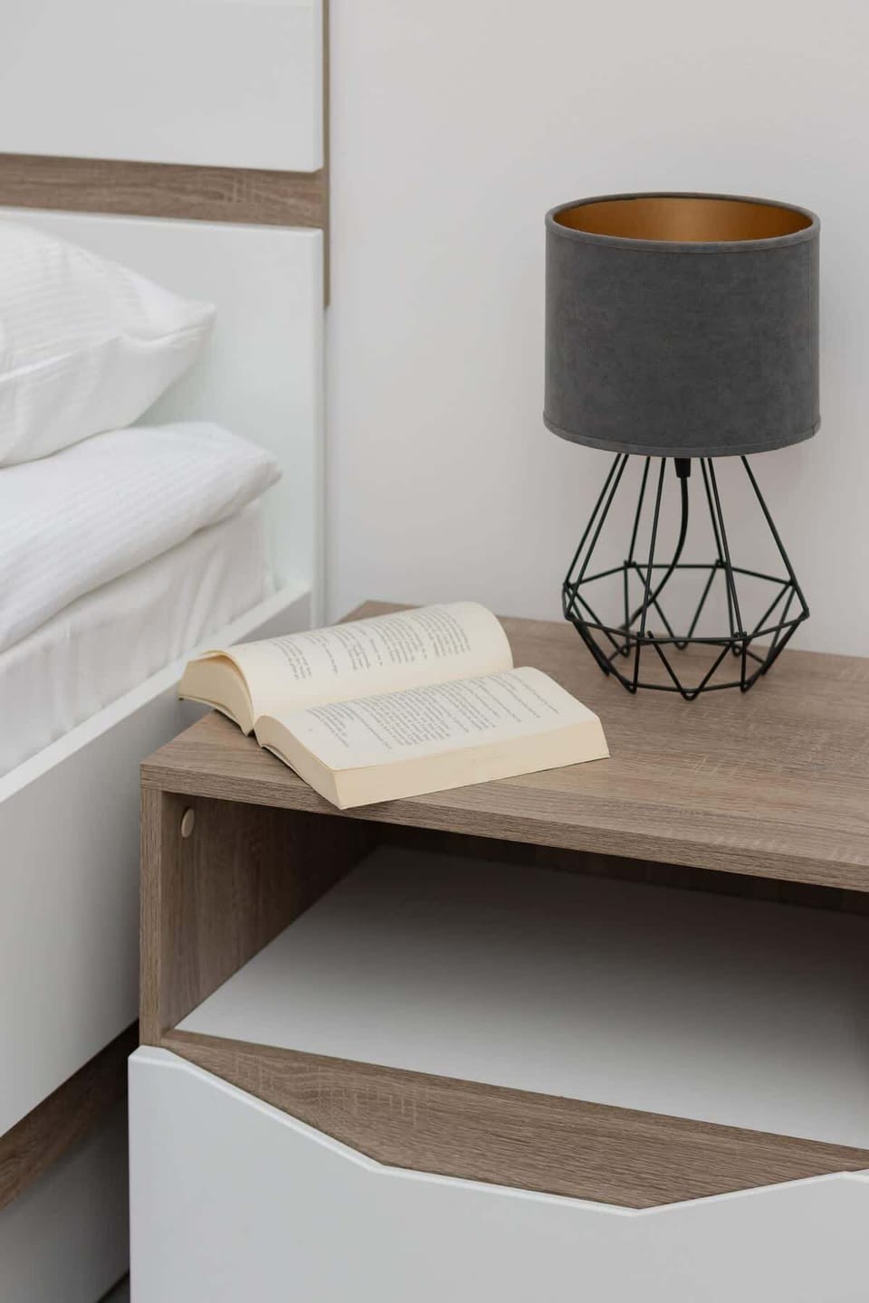 A stylish bedroom corner with a modern bedside table and lamp. Neutral colors and clean lines emphasize the minimalist design.