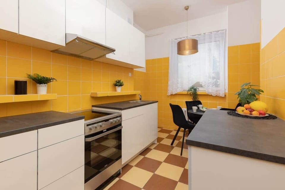 A modern kitchen with yellow and white cabinetry, a built-in oven, and a dining area. The space is bright and functional, perfect for cooking and gathering.