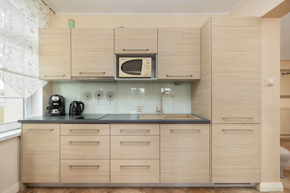 A modern kitchenette with wooden cabinetry, stainless steel appliances, and a glass backsplash, giving it a sleek and stylish look.