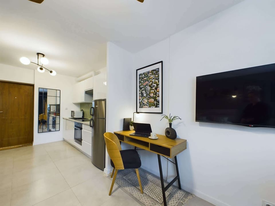 Cosy and stylish living area for three people with television, desk, dining table, kitchenette and wardrobe.