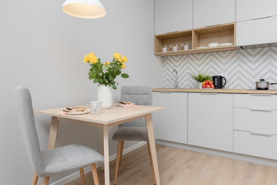 A small dining area with a round table and two chairs, decorated with a vase of vibrant yellow flowers, creating a cheerful atmosphere.


