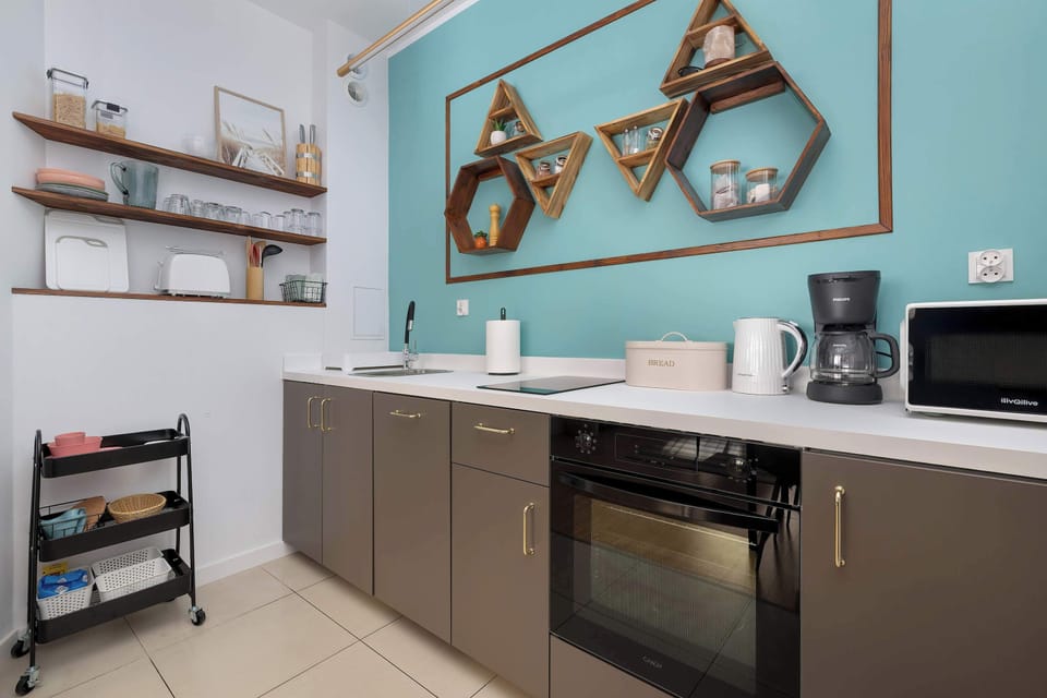 Modern kitchen with open shelves, turquoise wall, and built-in appliances.