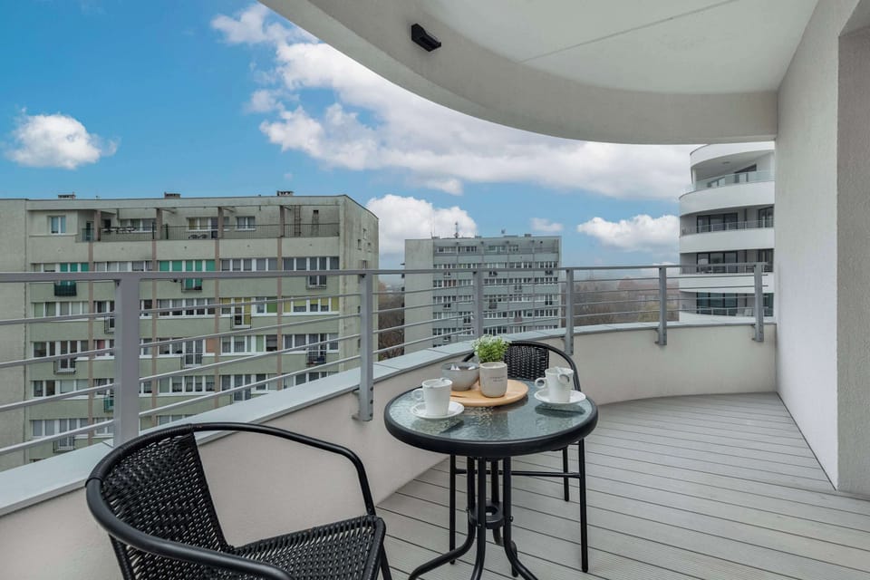 A spacious balcony with a small table and chairs, offering a stunning view of the surrounding city and buildings. Ideal for morning coffee or an evening drink.

