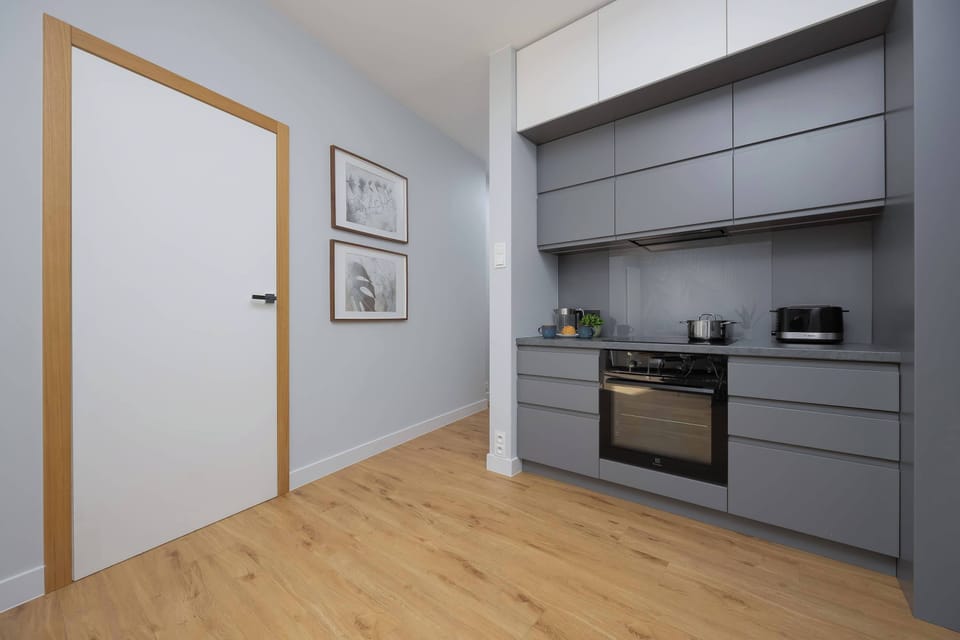 A stylish kitchen area with grey cabinets and a minimalist layout. The space is well-lit and features a clean, contemporary aesthetic.
