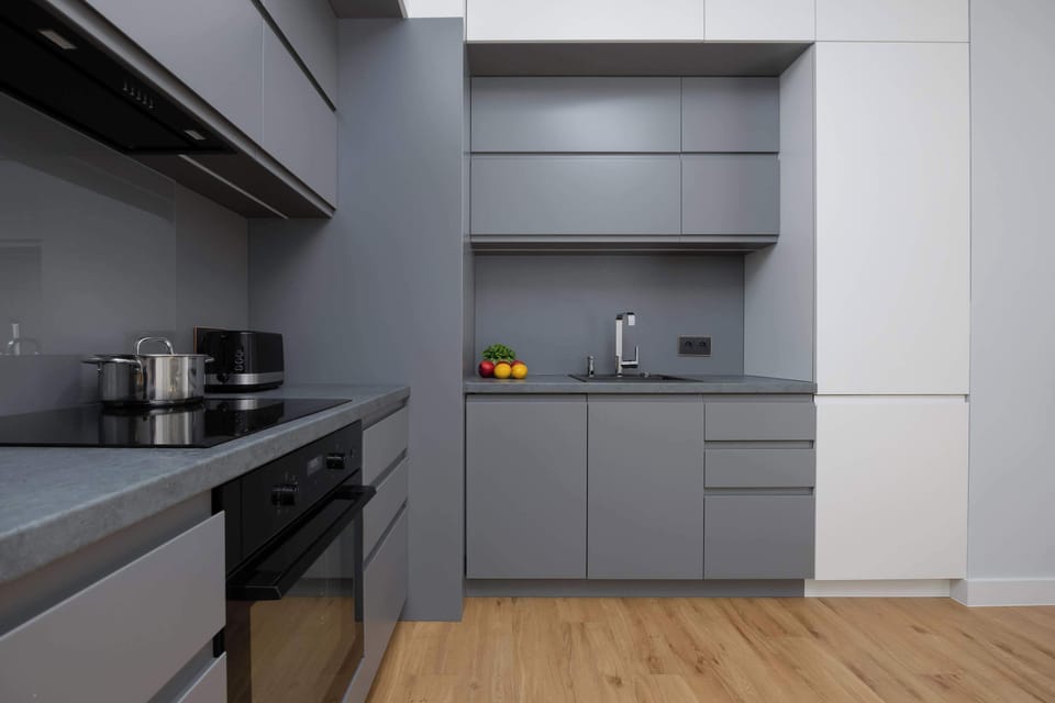 A sleek and modern kitchen with grey cabinetry, built-in appliances, and wooden flooring. The space is compact yet functional with a minimalist design.