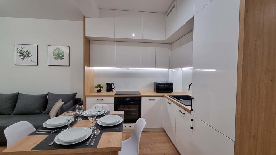  A small, modern kitchen with white cabinets, wooden countertops, and a dining table set for four. The kitchen has all essential appliances and a neat, organized layout.