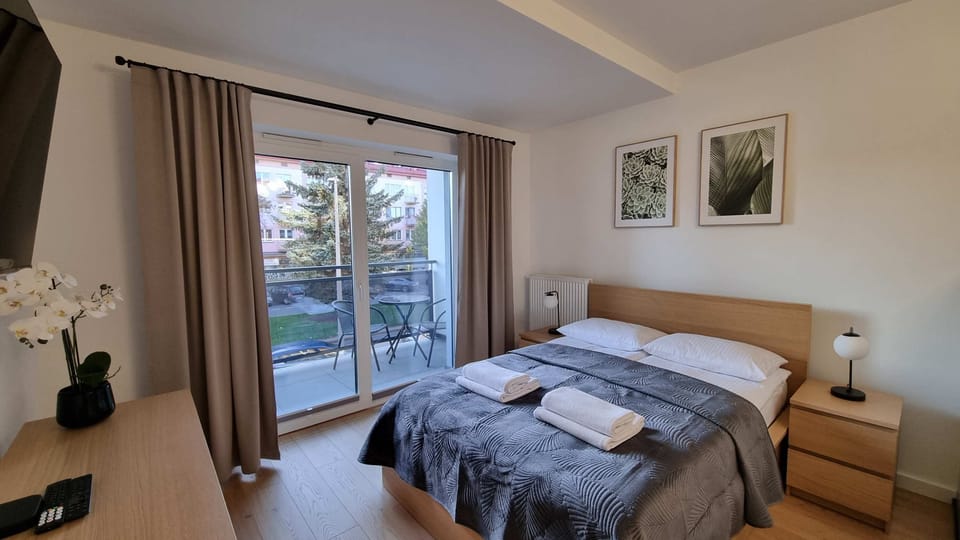  A different angle of the bedroom showing a large window with curtains. The bed is neatly made, and the room features modern decor, including framed pictures above the bed.
