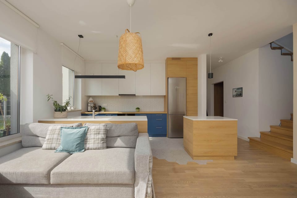 A spacious and stylish living room in light colors of gray and beige with a modern kitchenette and a comfortable upholstered sofa.
