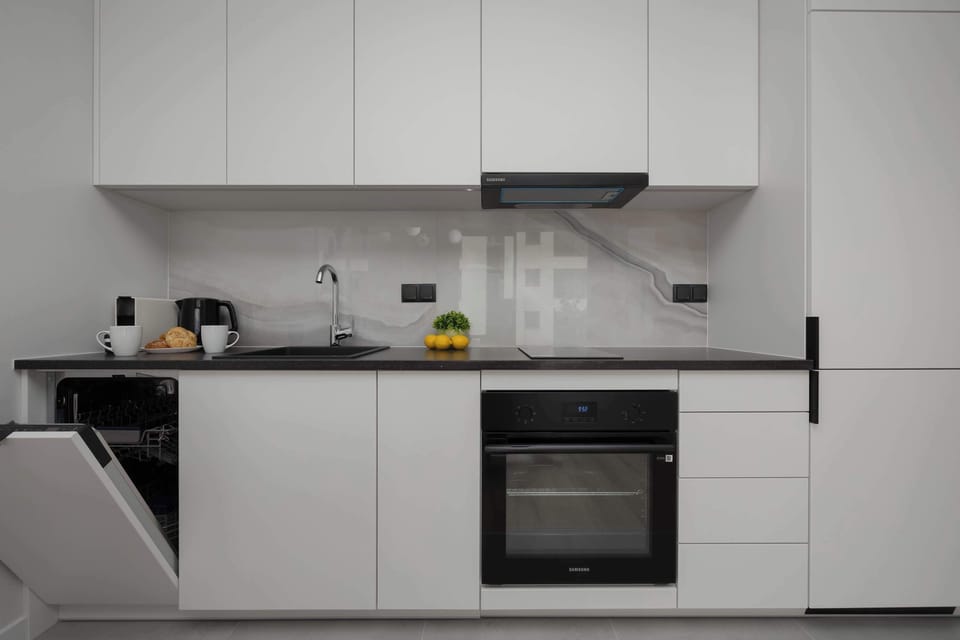 A functional kitchenette with white cabinets, contrasting black handles, and a modern oven and cooktop combines aesthetics with practicality.