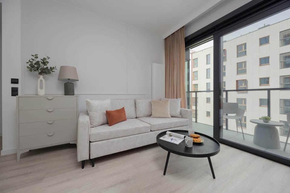 A modern living room featuring a light-gray L-shaped sofa, black round coffee table, and a view onto the balcony.