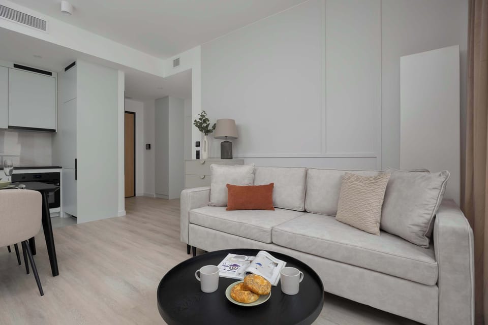 A spacious and bright living area with a soft-toned sofa, minimalist furnishings, and a cozy ambiance.

