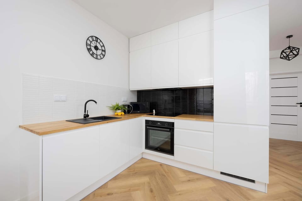 The kitchen from a slightly different angle, focusing on the minimalist white cabinets and black backsplash.