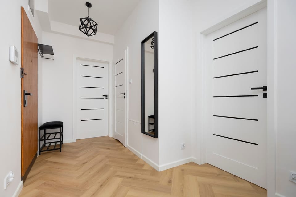A hallway with white doors, light wooden flooring, and minimalist interior lighting.