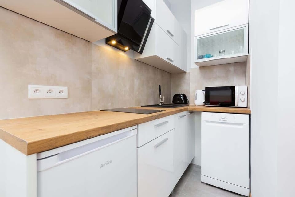 A kitchen space with white cabinets and wooden countertops, adjacent to a small dining table with chairs. The setup is compact yet functional.