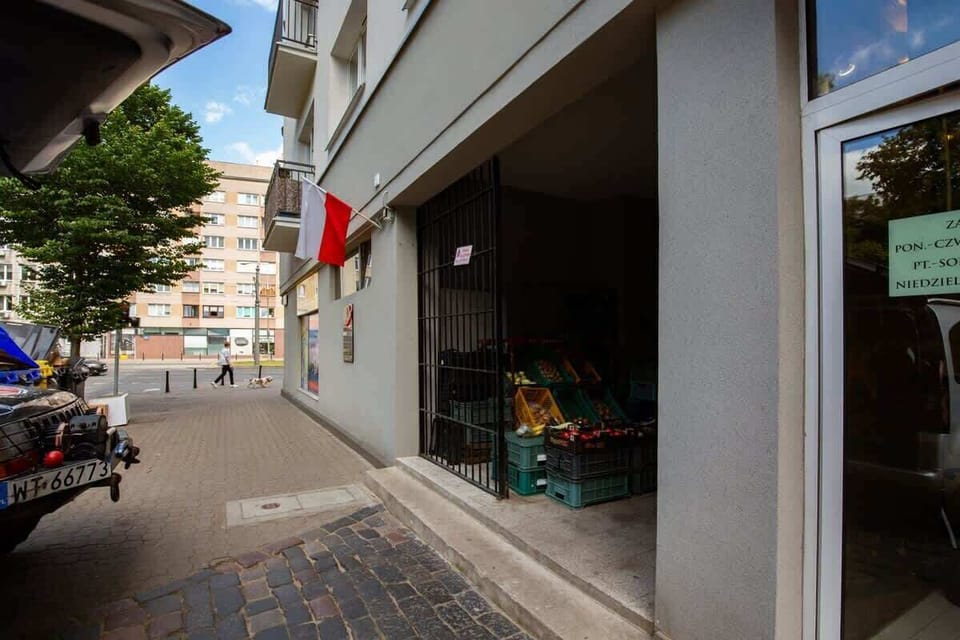 The entrance to an apartment building, with a modern facade and a small outdoor seating area nearby.