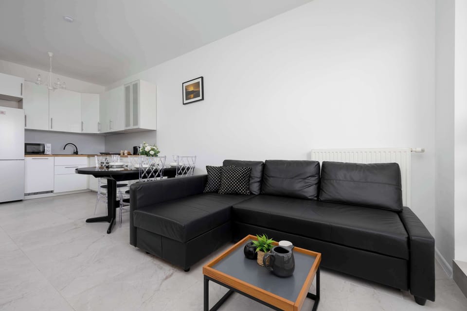This living area features a spacious, modern black sofa, a stylish coffee table, and a minimalist decor that adds a touch of elegance to the room.