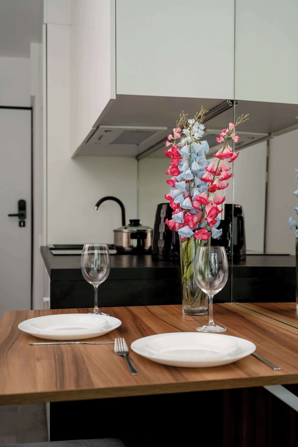 Dining table with tableware and kitchenette in the background.