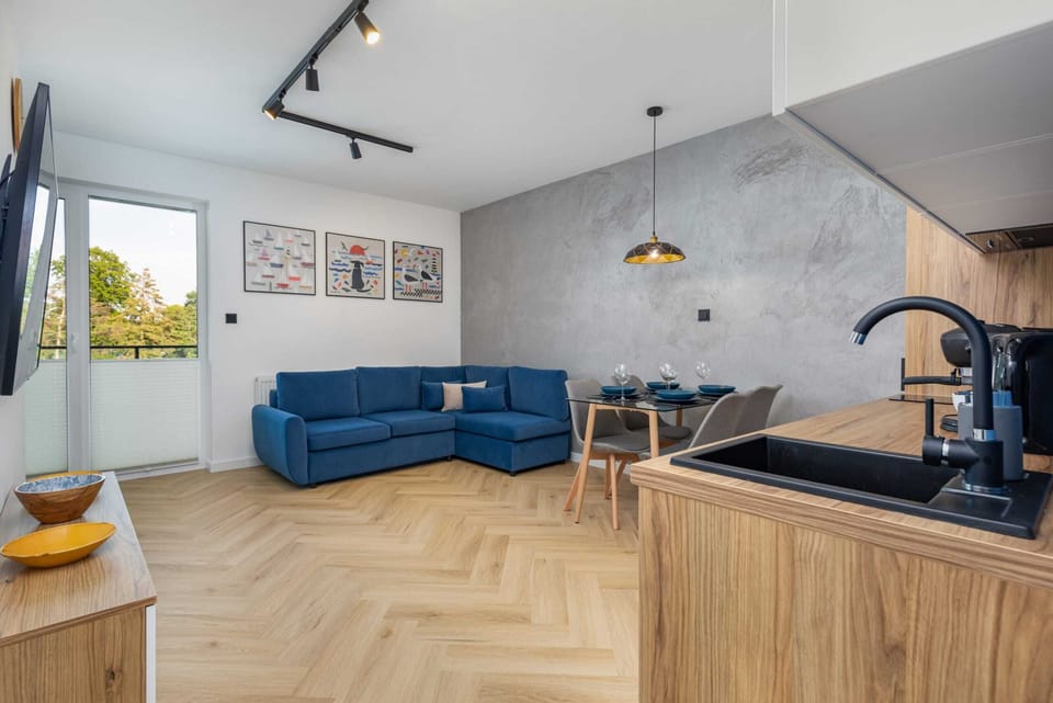 An open-plan living area with a modern kitchenette, dining space, and stylish blue sofa.
