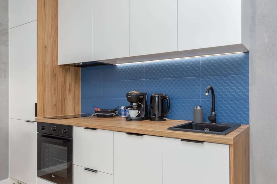 A functional kitchenette with white cabinets, a blue backsplash, and modern appliances.
