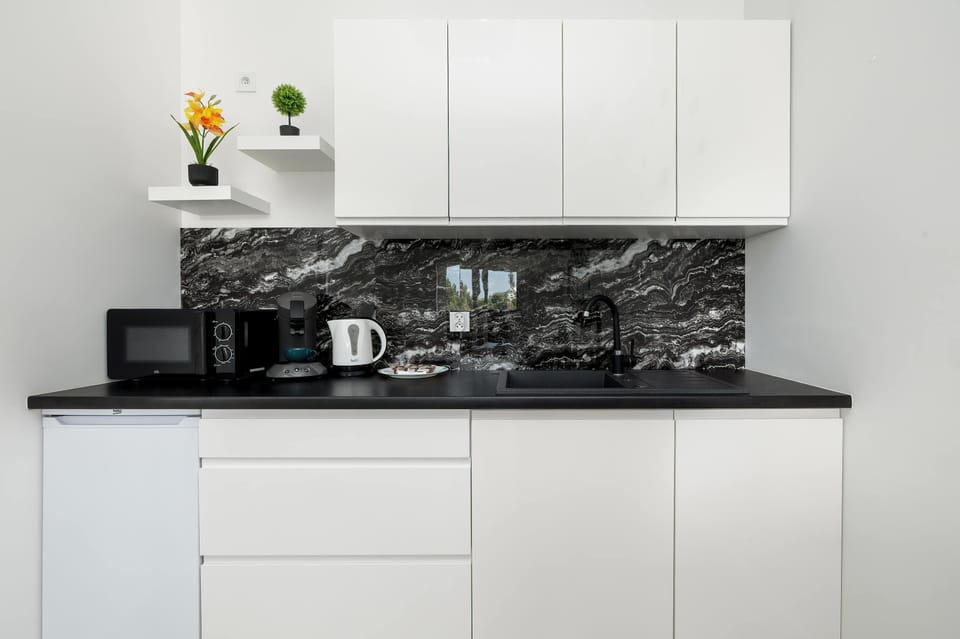 A minimalist kitchen area featuring white cabinetry, a black mosaic backsplash, and compact appliances including a kettle and coffee maker.