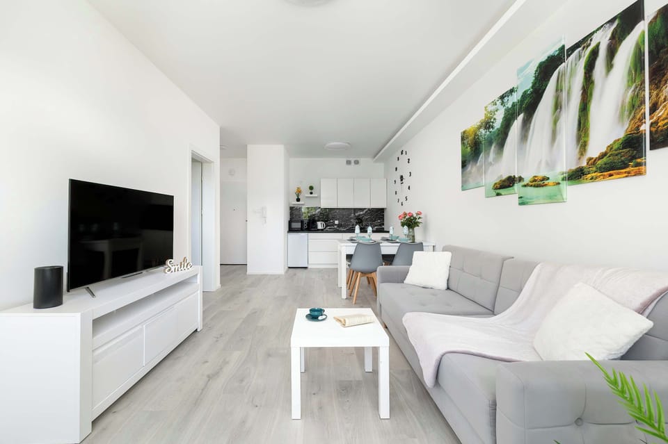 An open-plan view combining a modern kitchen with high-gloss cabinets and a living room with TV and balcony access.