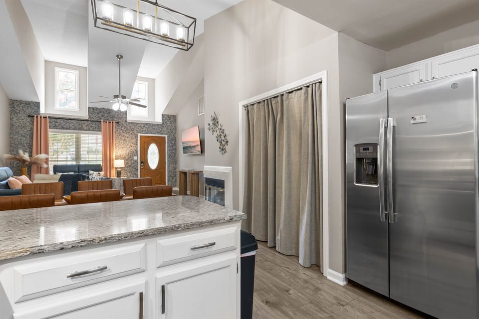 Bright and stylish view from the kitchen featuring granite countertops, stainless steel fridge, and a peek into the cozy living area with high ceilings and natural light.