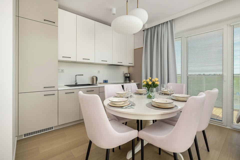 A dining area with pink velvet chairs, a round table set for meals, and a window providing abundant natural light.