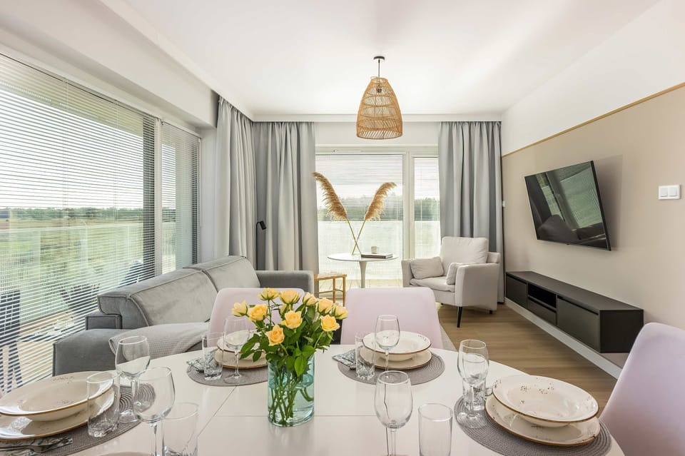 A modern living area with a soft color palette, gray furnishings, and natural light flooding in through large windows.