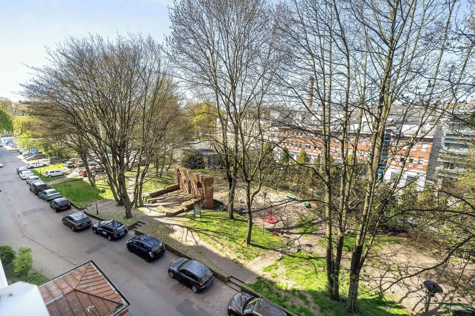 The view from the apartment window overlooks a playground with large trees.