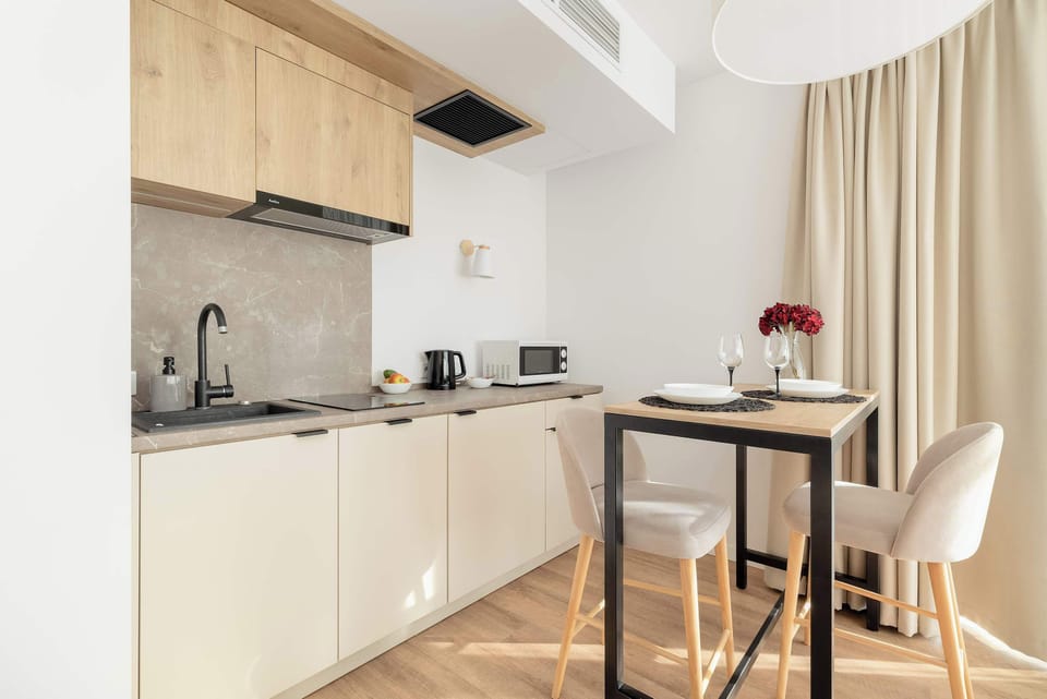 An open kitchen and dining area with minimalist design. The light wood cabinets and white countertops create a clean, modern aesthetic.