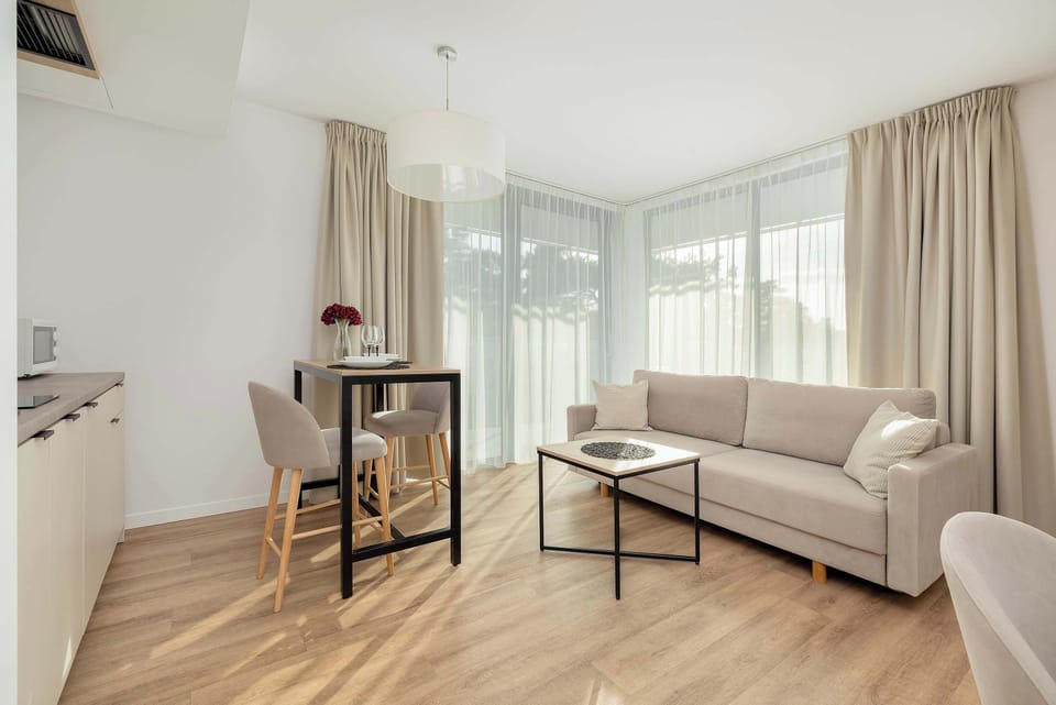 This modern living room features a comfortable sofa facing a large window, offering direct access to a balcony. The mix of soft textures and natural light creates a welcoming environment with a great connection to the outdoor space.