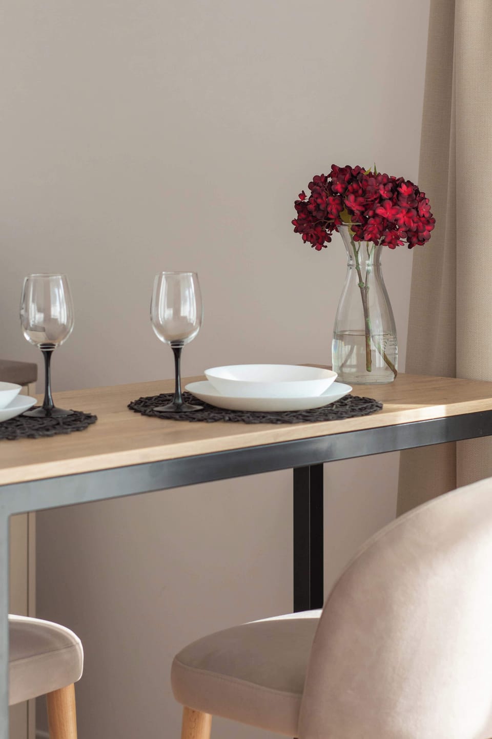 A close-up view of a dining table set with plates and glasses. A vase filled with red flowers serves as a beautiful centerpiece, adding a pop of color to the otherwise neutral setting.