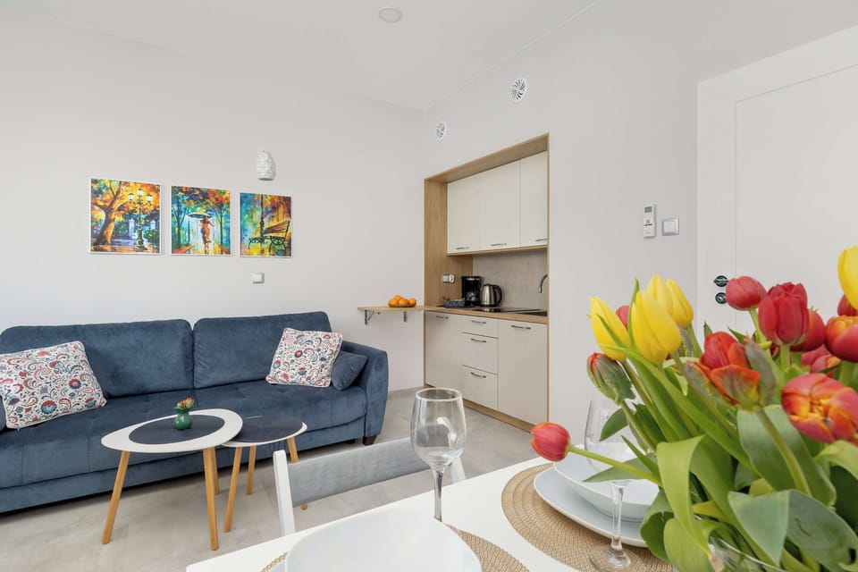 A sitting area with a blue sofa and a small round table. Colorful flowers in the foreground add warmth. The layout feels inviting and thoughtfully styled.