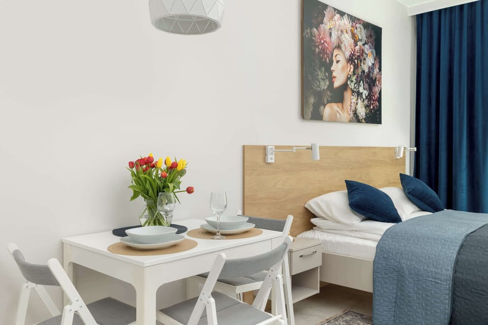 A bedroom corner with a bed placed next to a small dining table. Blue curtains and soft lighting create a relaxing mood. The space feels practical and well arranged.