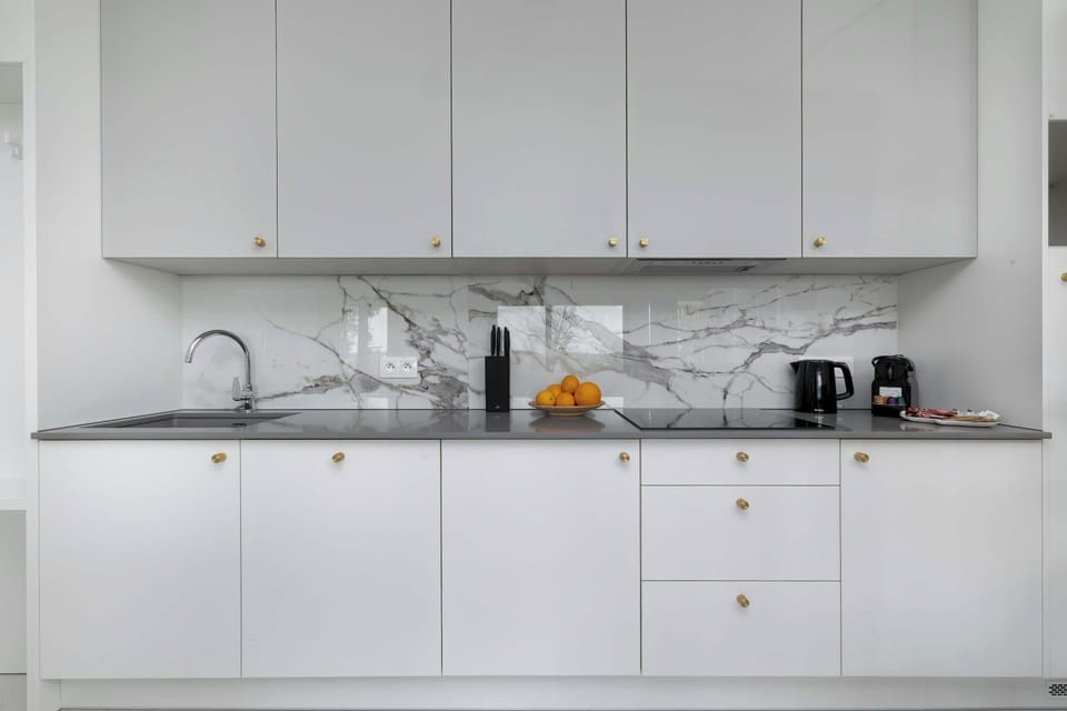 A sleek, white kitchen with clean lines and built-in appliances. The countertop is clutter-free and ideal for cooking or dining.