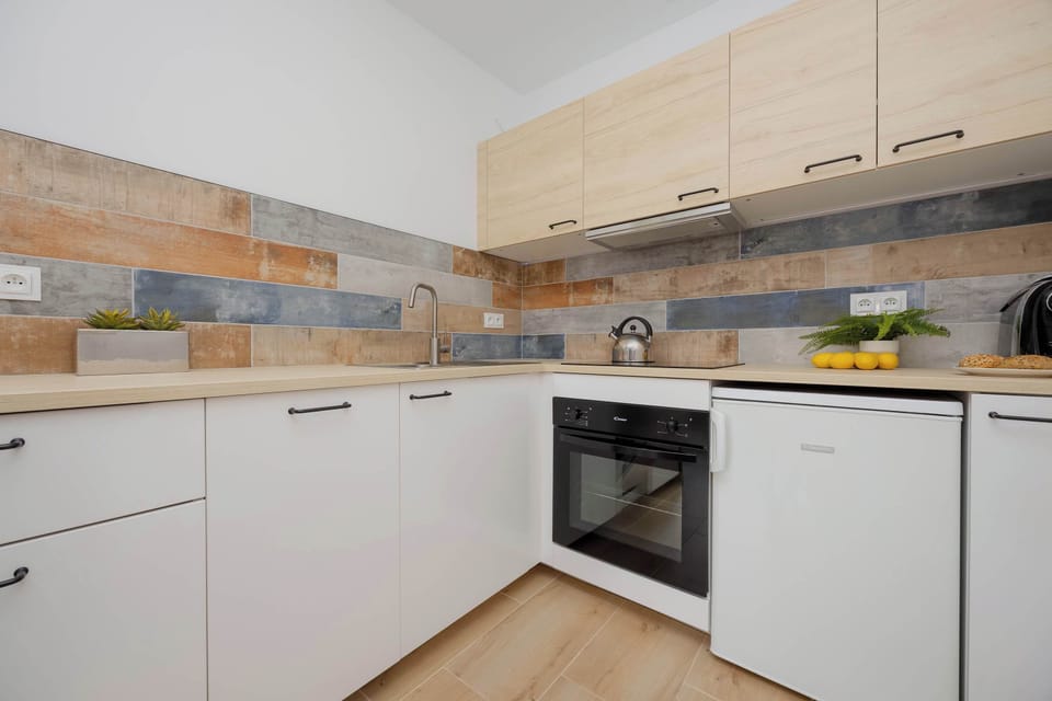 Well-lit kitchenette with white cabinets, wooden countertops, and a dining setup decorated with flowers.