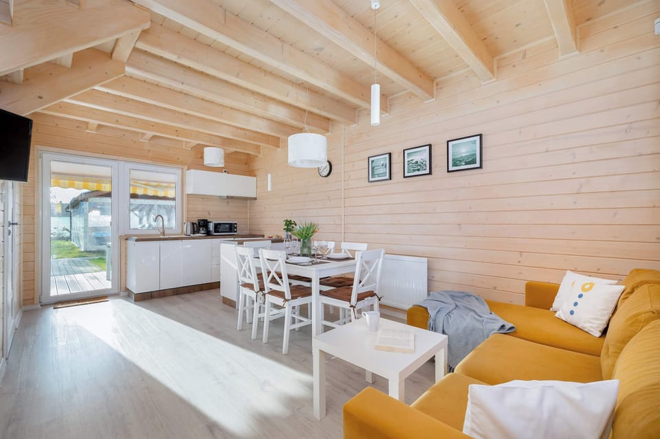 Bright living room with wooden walls, yellow curtains and sofa, white table and chairs.