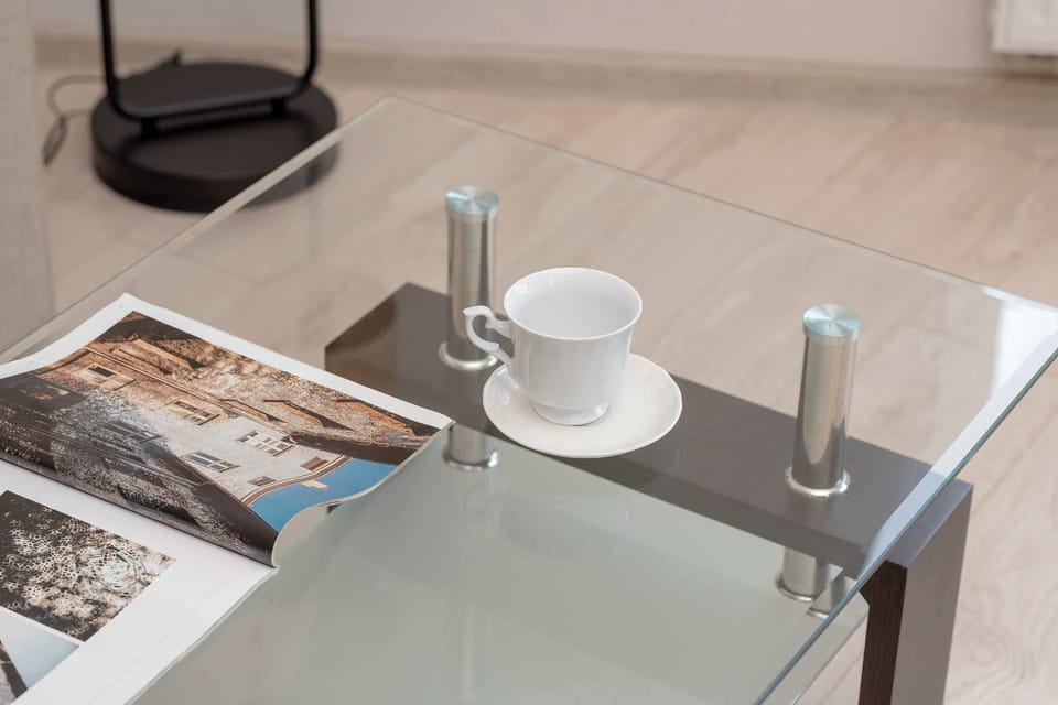 On the glass table are cups on saucers, a book and a set of toiletries, suggesting that this may be a seating area.