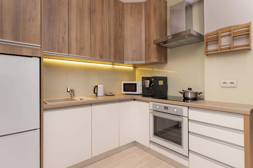 A modern kitchen with light wooden cabinets. You can see the oven, hob and other kitchen appliances such as the coffee machine and microwave. The whole creates a perfect space for preparing meals. 
