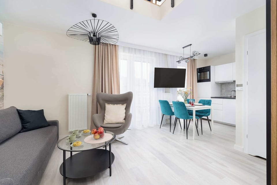 Spacious living room with a gray sofa, coffee table, armchair, television and kitchenette with dining area.
