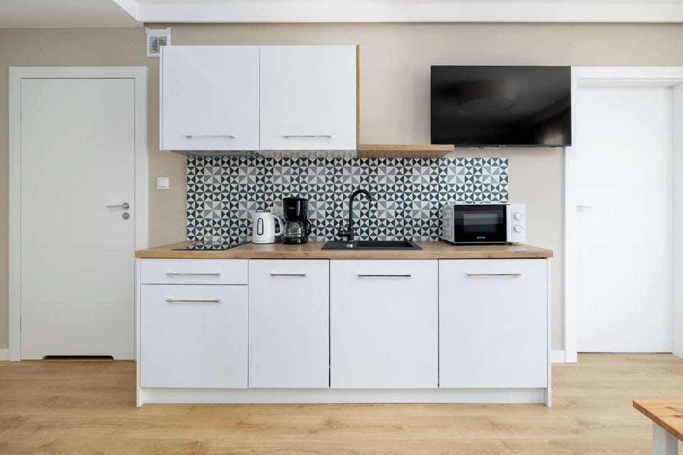 A modern kitchen with white cabinetry, black-and-white geometric backsplash, and built-in appliances. Minimalist design with open space for cooking and entertaining.