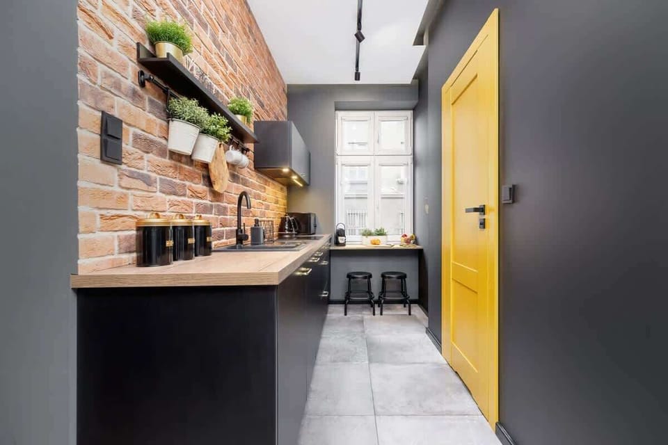 A compact kitchen with black cabinets and wooden shelves, filled with plants and utensils, creating a warm and rustic atmosphere.