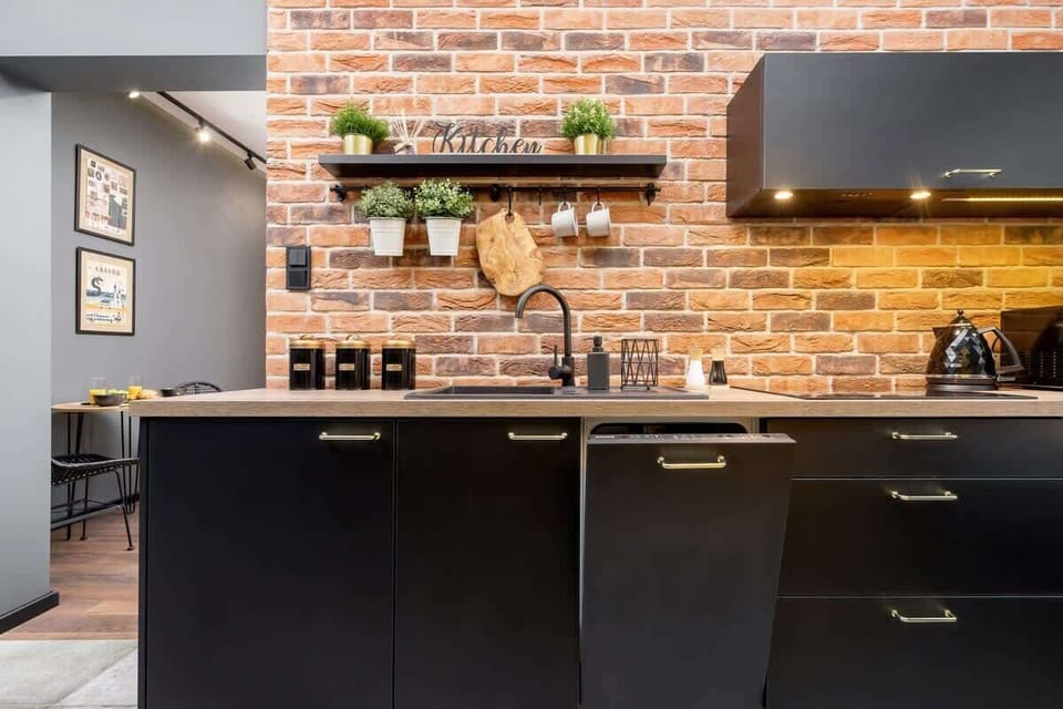 Funkcional kitchen with black cabinets and wooden shelves, filled with plants and utensils, creating a warm and rustic atmosphere.