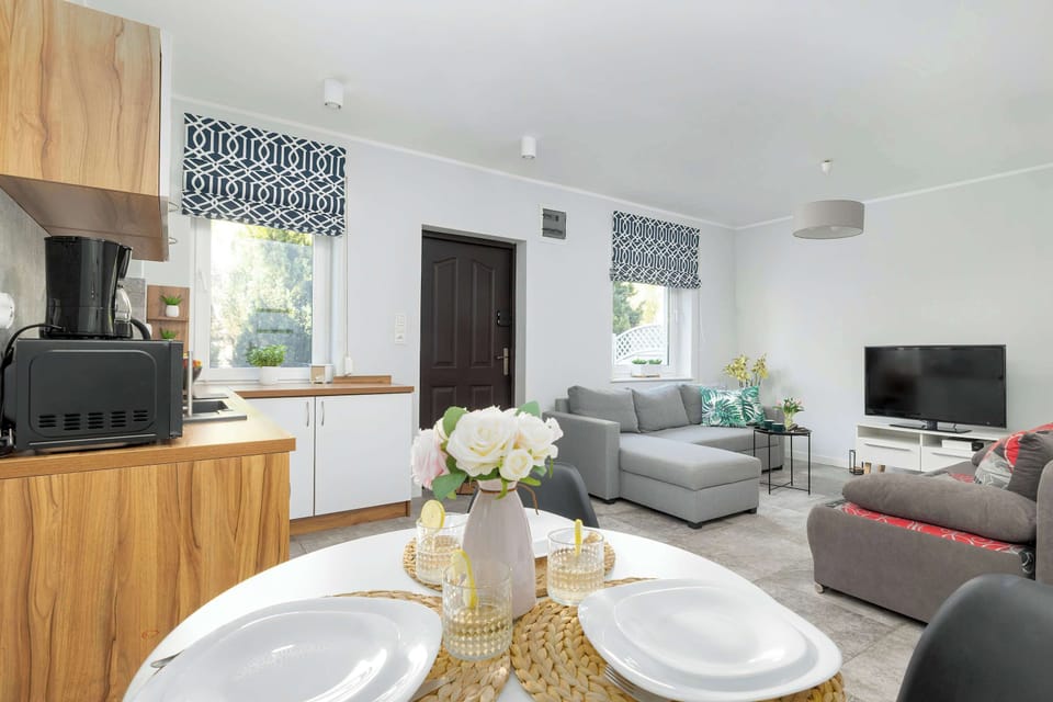 A dining table with a place setting for 3 people and a bouquet of flowers, and decorative white and black blinds on the windows.