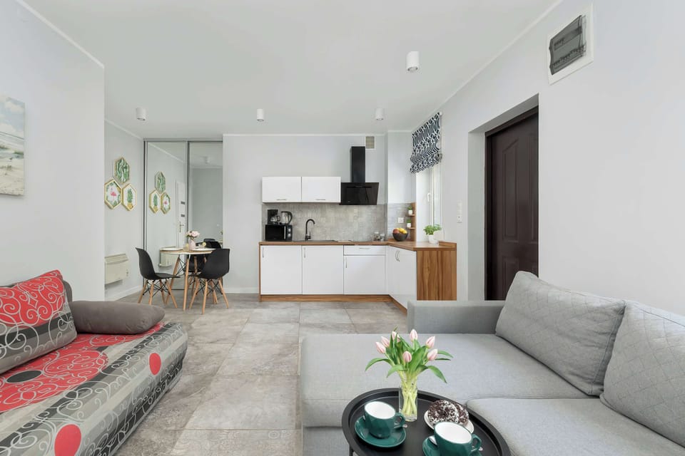 Studio in a muted light gray color scheme with coffee table, sofa and corner sofa, dining table and kitchenette.
