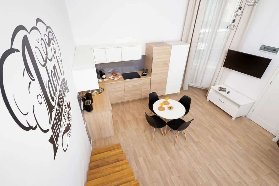 A modern open-plan kitchen with black and wooden cabinetry, a dining table, and stylish wall decor.