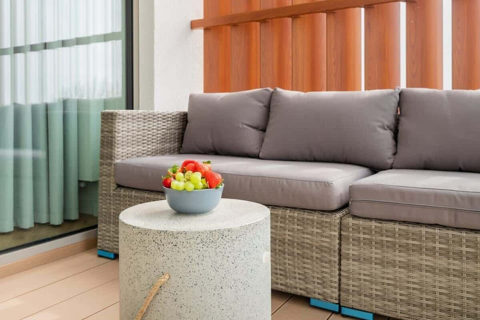 A spacious balcony featuring comfortable seating, wooden privacy paneling, and a small side table.