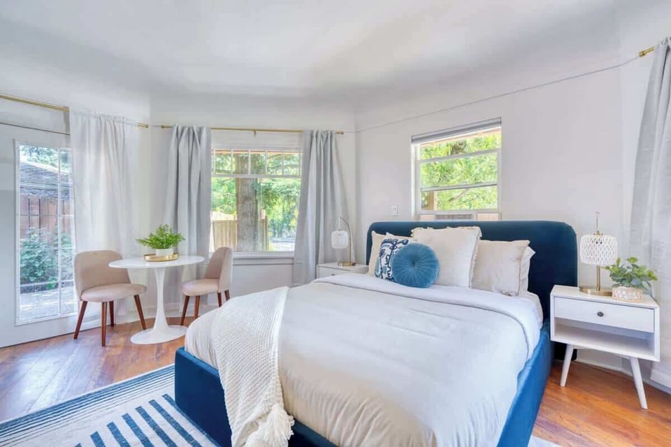 Bed beside three windows and a small two-chair table.