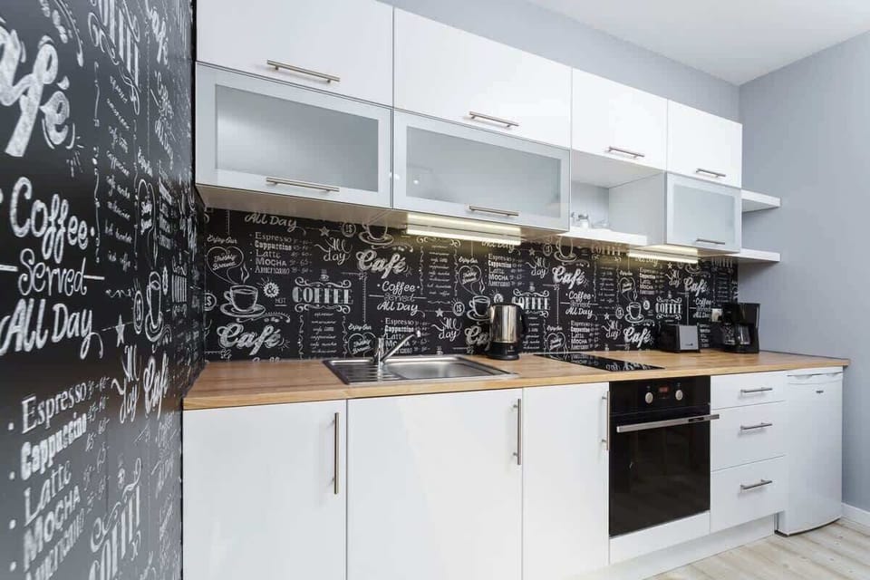 A bright kitchen with white countertops, cabinets, and wooden finishes, with a window in the background.